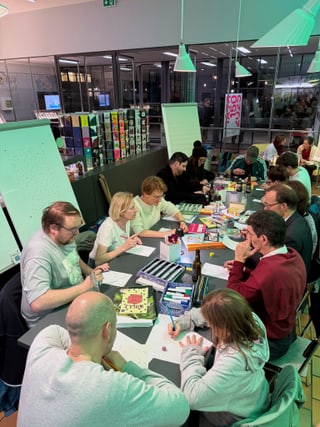 Gruppe von Menschen bei einem Schreibworkshop an einem Tisch mit Schreibmaterialien.