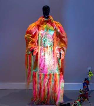 Mannequin in buntem, flauschigem Kleid vor grauer Wand.