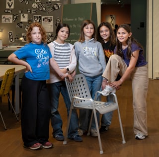 Fünf Kinder posieren in einem Raum mit Tafeln und Stühlen.