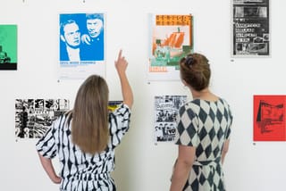 Zwei Personen betrachten Poster an einer weissen Wand.