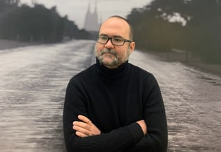 Mann mit Bart steht vor verschwommener Strasse und Bäumen im Hintergrund.