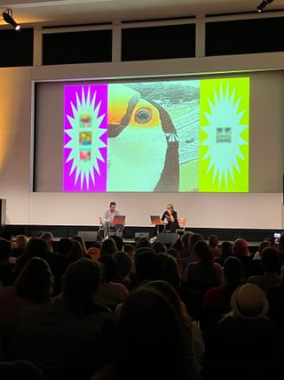 Präsentation vor Publikum mit buntem Bild auf Bildschirm.