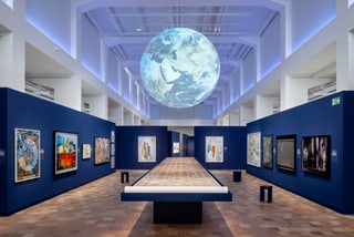 Kunstgalerie mit ausgestellten Gemälden und einer Erdkugelinstallation an der Decke.