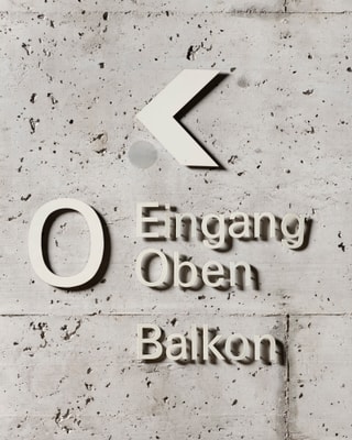 Beschilderung auf Betonwand mit Pfeil und Text Eingang, Oben, Balkon.