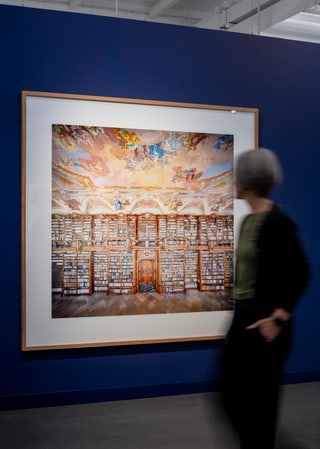 Person betrachtet grosses Gemälde einer Bibliothek an blauer Wand.