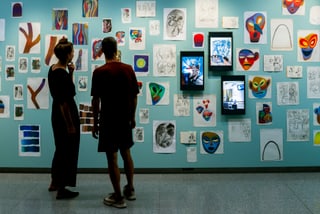 Zwei Personen betrachten Kunstwerke an der Wand.
