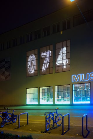 Nachtaufnahme eines Gebäudes mit leuchtenden Zahlen 074 im Fenster.