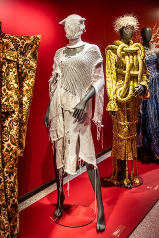 Schaufensterpuppen mit avantgardistischer Mode vor rotem Hintergrund.