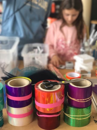 Bunte Klebebänder und Schere auf einem Tisch mit einem Kind im Hintergrund.