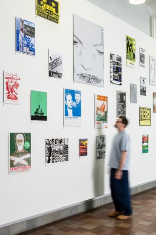 Person betrachtet eine Wand mit Postern in einer Ausstellung.