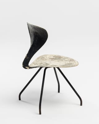 Skulpturartiger Stuhl mit geschwungener Rückenlehne und Metallbeinen.