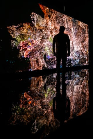 Person steht vor leuchtendem Kunstwerk mit Spiegelung im Boden.