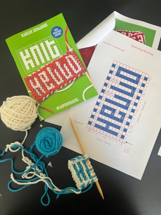 Strickbuch mit Garn, Nadeln und Musterdiagramm auf Tisch.