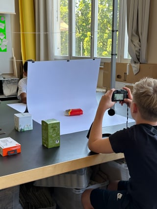 Junge fotografiert Produkt auf Tisch im Klassenzimmer.