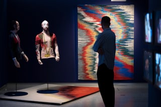 Person betrachtet Kunstinstallation mit Figuren und Wandteppich.