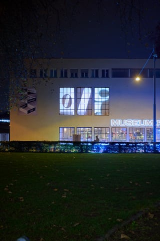 Nachtansicht eines beleuchteten Museumsgebäudes mit Rasen im Vordergrund.