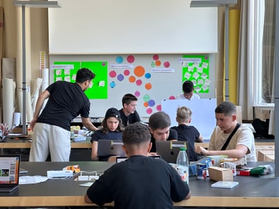 Schüler arbeiten in einem Klassenzimmerprojekt mit Laptops und Bastelmaterialien.