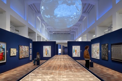 Kunstausstellung mit Gemälden in blauem Raum, grosse Kugel an der Decke.
