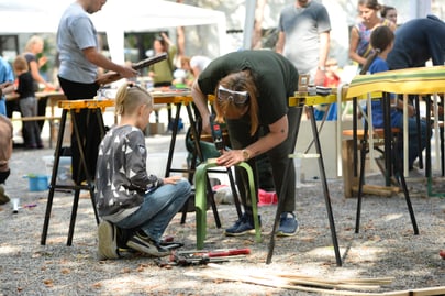 Erwachsene und Kinder arbeiten draussen an Stühlen aus Holz.