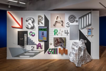 Kunstinstallation mit Buchstaben und geometrischen Formen an einer Wand, grosser Stein davor.