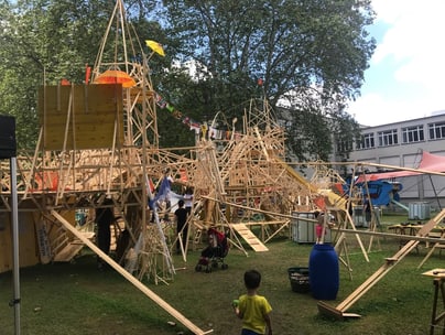 Holzstruktur auf einem Festivalgelände mit Kind im Vordergrund.",