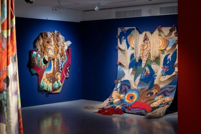 Kunstinstallation mit bunten Textilien an einer blauen Wand.