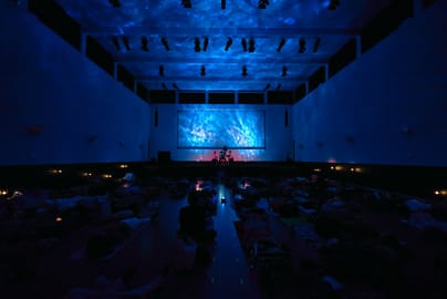 Dunkler Raum mit Projektionsleinwand und blauer Beleuchtung.