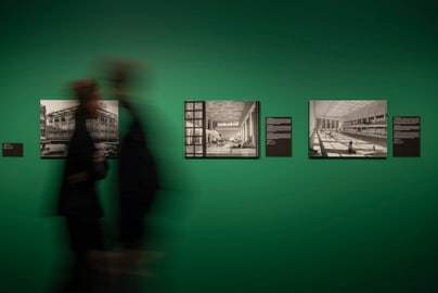 Zwei unscharfe Personen vor grüner Wand mit schwarz-weissen Fotos.