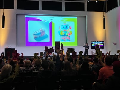 Menschenmenge hält Schilder vor Bildschirm bei Präsentation in Auditorium.