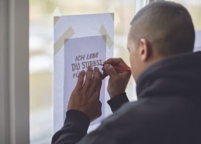 Person schreibt an ein Fensterplakat.