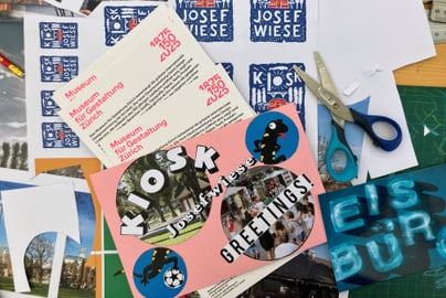 Collage mit Postern, Fotos und Schere auf Tisch verteilt.