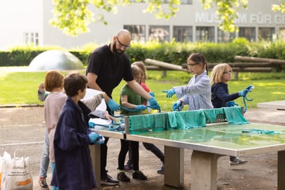 Kinder und Erwachsener bei einem Outdoor-Kunstprojekt mit gefärbten Stoffen.