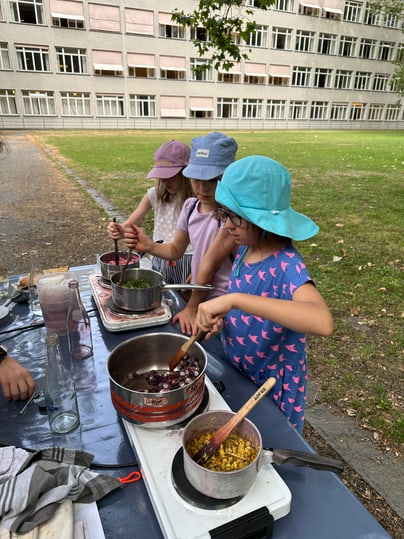 Kinder kochen natürliche Farben ein draussen auf einem Tisch vor einem Gebäude.",