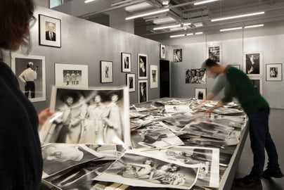 Menschen durchsuchen Stapel von Schwarzweissfotos in einer Galerie.