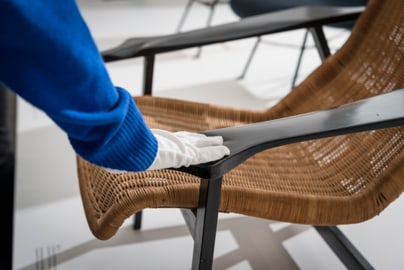 Hand mit Handschuh berührt Korbstuhlarmlehne.