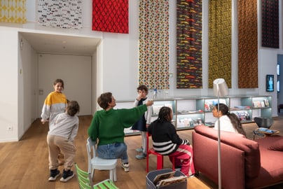 Kinder und Erwachsener in hellem Raum mit bunten Wandteppichen.