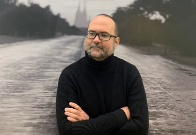 Alejandro Cartagena steht vor schwarzem Hintergrund mit verschwommener Landschaft.