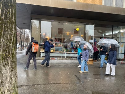 Menschen mit Regenschirmen gehen an einem Geschäft vorbei.