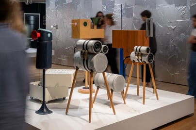 Kunstinstallationen auf Podest in Galerie mit Besuchern.