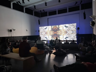 Menschen im dunklen Raum schauen auf eine beleuchtete Leinwand mit abstrakten Mustern.