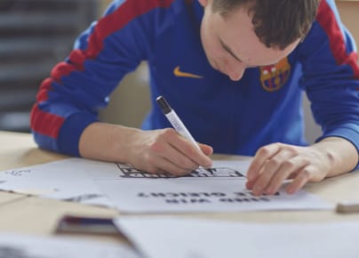 Mann in blauem Sweatshirt schreibt auf Papier auf einem Tisch.
