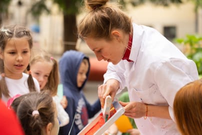 Erwachsene Frau zeigt Kindern handwerkliche Tätigkeit des Siebdrucks im Freien.