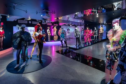 Bunt beleuchtete Ausstellung mit auffälligen Kostümen auf Schaufensterpuppen.