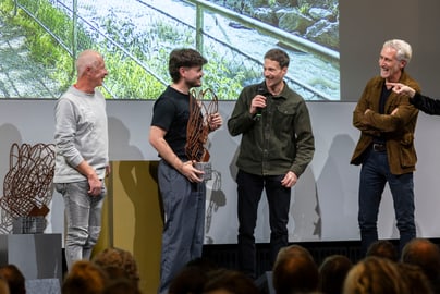 Vier Männer auf einer Bühne bei einer Preisverleihung, halten eine Skulptur hoch.