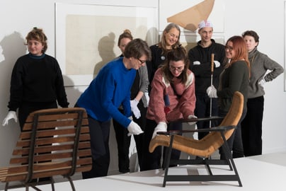 Gruppe von Menschen betrachtet Stuhl in Ausstellungsraum.