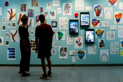 Zwei Personen betrachten Kunstwerke an der Wand.