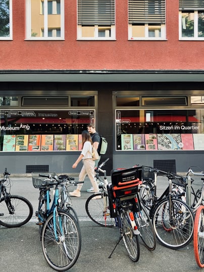 Menschen gehen an geparkten Fahrrädern vorbei vor dem Schaufenster der Schaufenster der Ausstellung im Quartier DesignScouts Schaufenster: Sitzen im Quartier