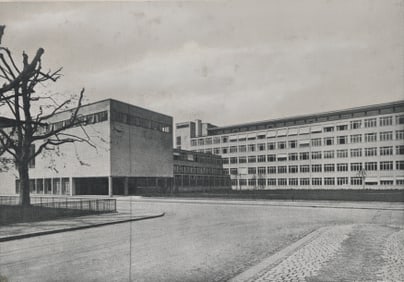 Schwarzweissfoto eines grossen Gebäudekomplexes mit kahlem Baum davor.