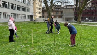 Kinder und Erwachsener in einem Park mit Pfosten und Seilen auf Gras.",