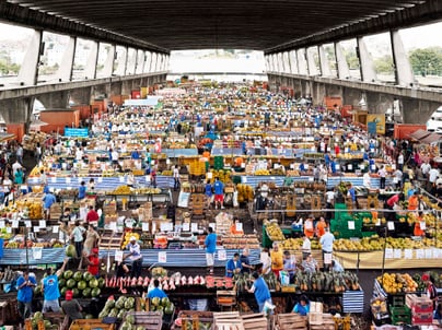Voller Markt unter überdachter Struktur mit verschiedenen Ständen und Menschen.